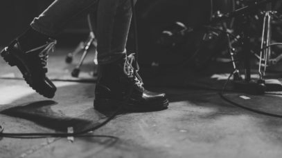 headphonik – person in black leather boots walking beside of drum set – Photo by Alex Brisbey